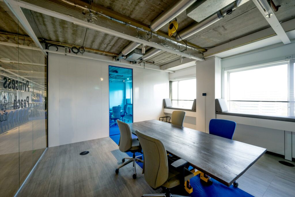 Vergaderruimte aan de Johan Huizingalaan met modern interieur, glazen wand en zicht op een aangrenzende blauwe kamer.